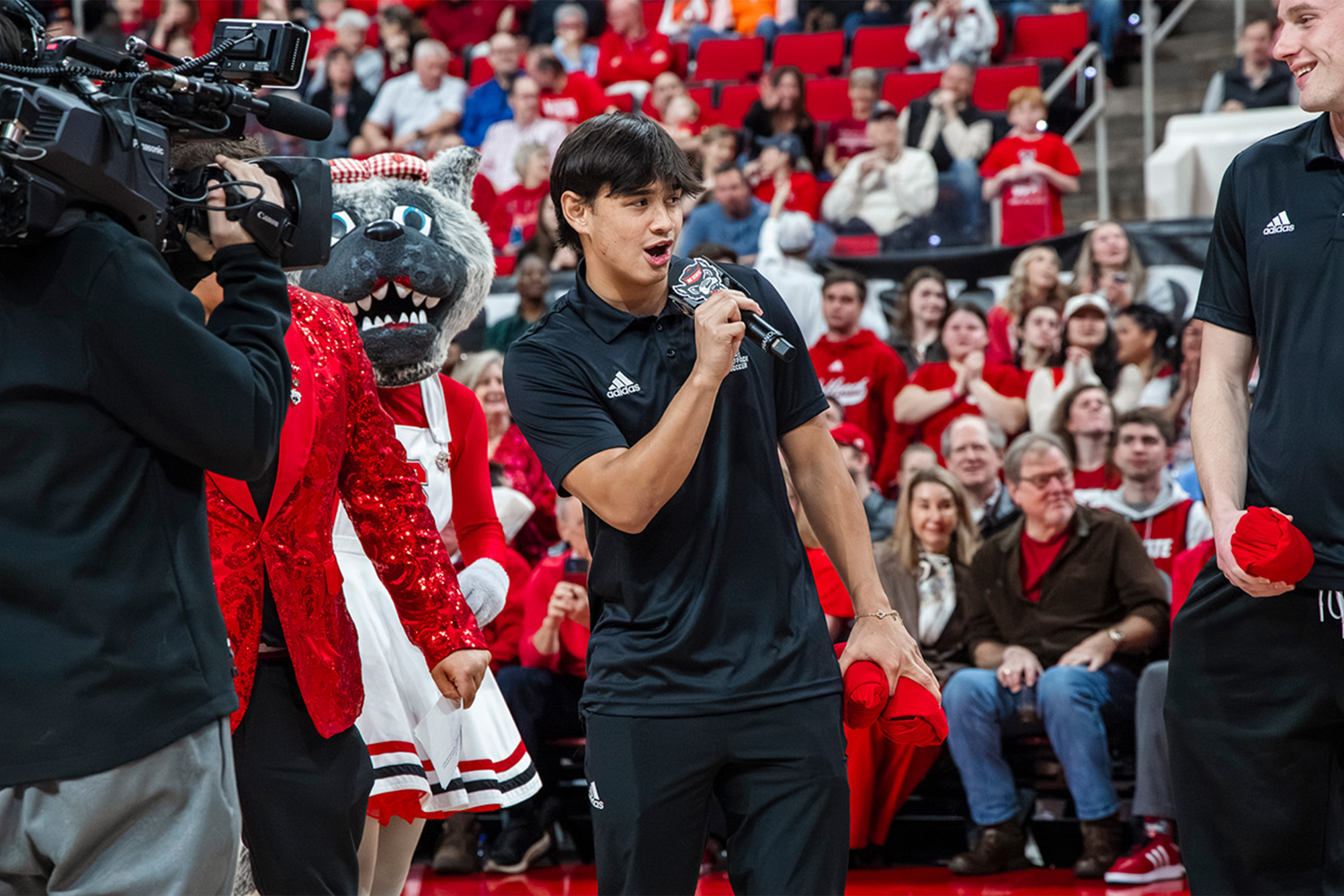 Caleb Tolentino speaking at a basketball game.