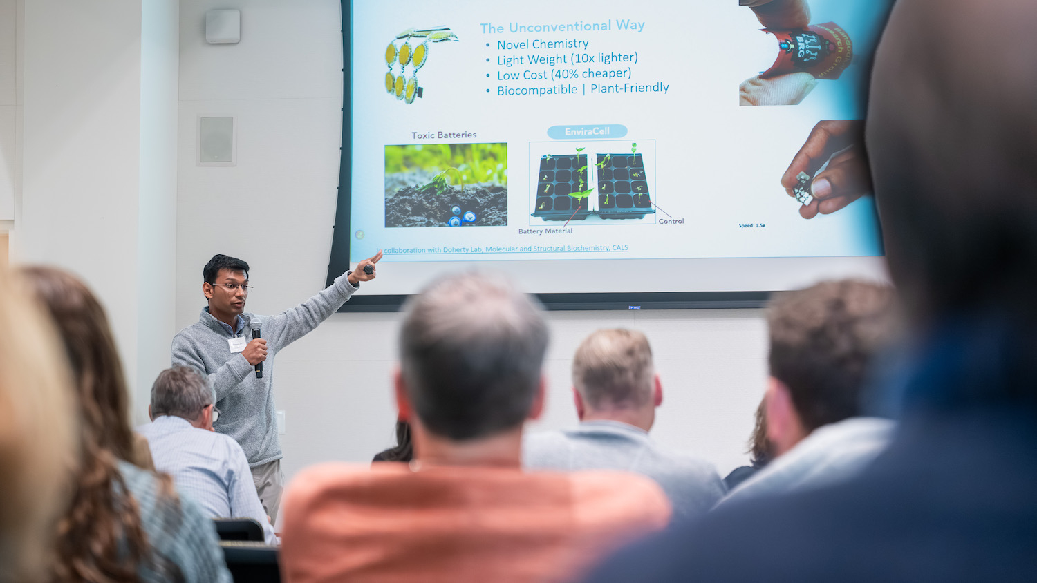 Before an audience, a man points to a slide projection to make a point about his battery technology.