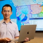 Individual holding laptop in front of a digital map display on screen, representing data analysis or geographic information.