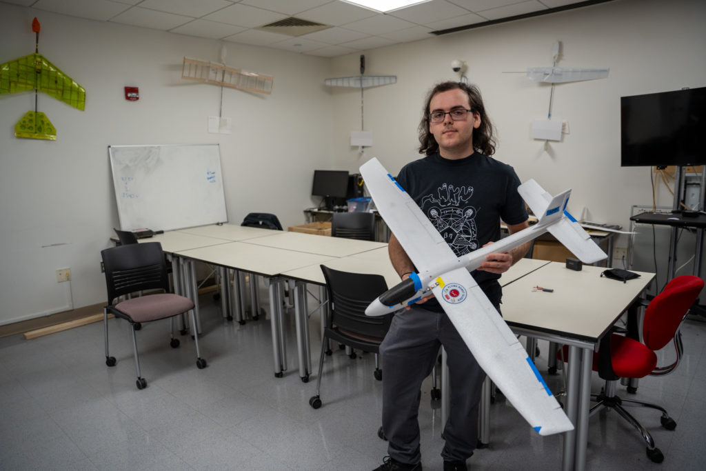 Person holding model airplane in classroom with model planes on walls.