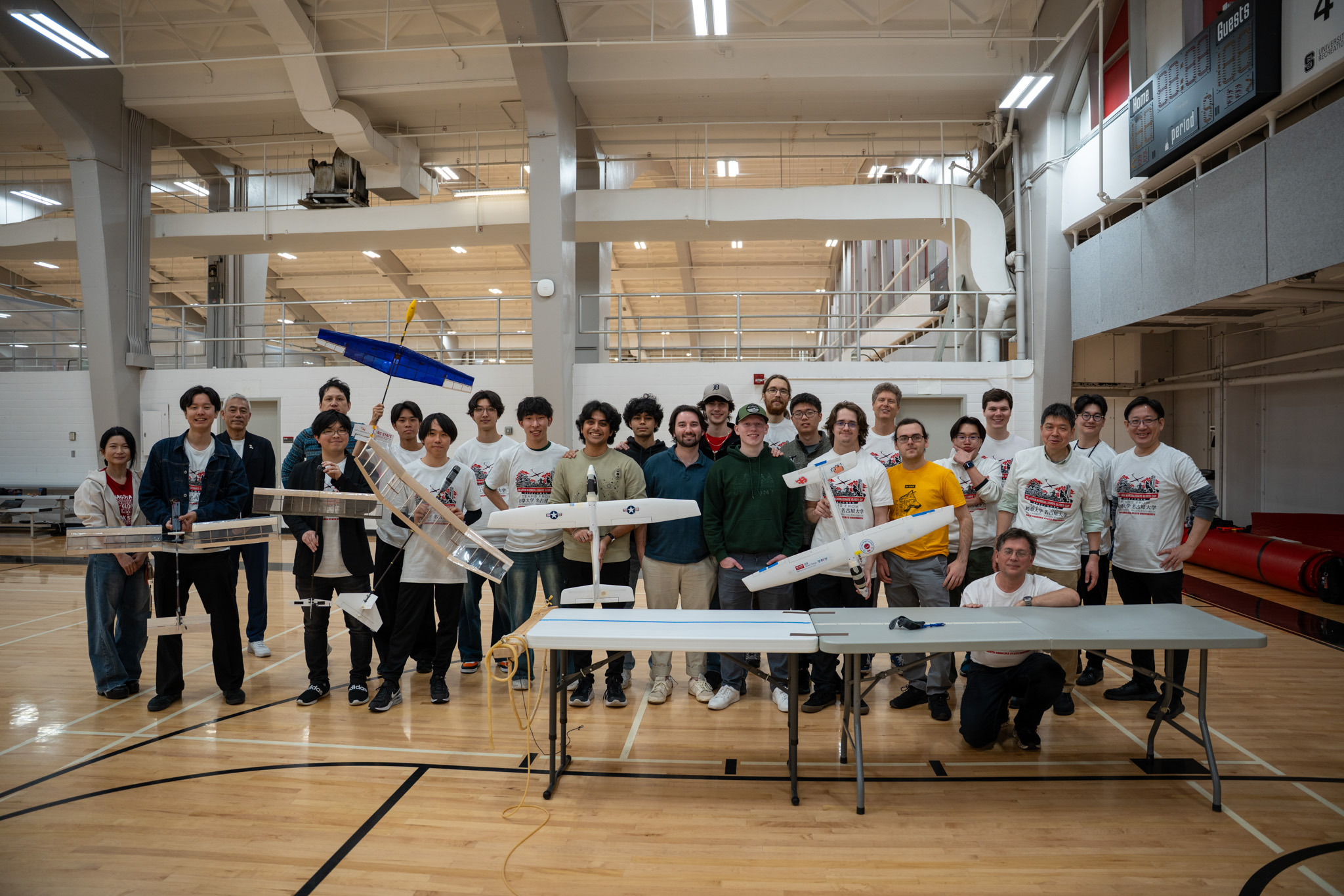 Group of students displaying model airplanes in an indoor sports facility.
