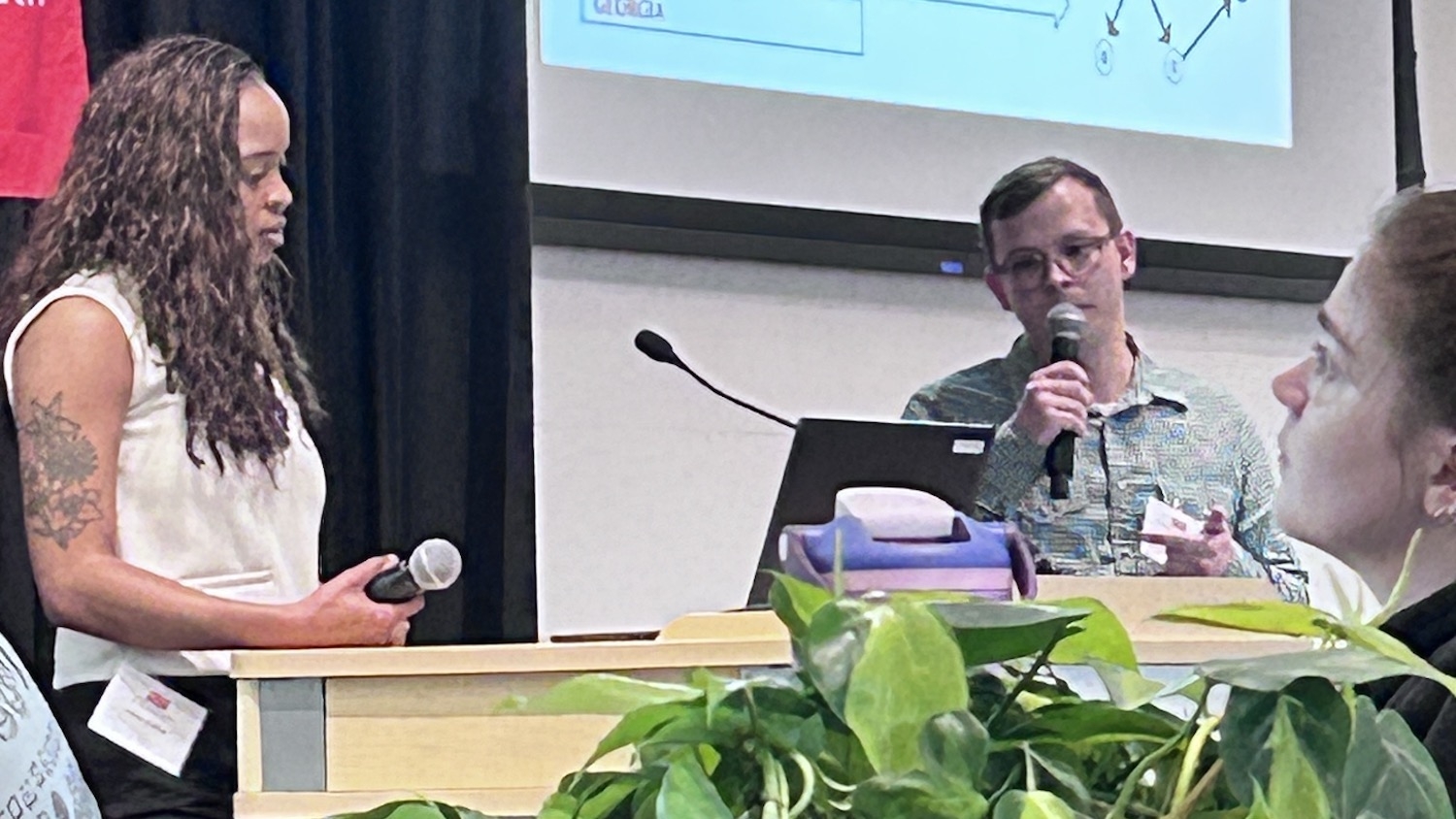 Two students, one speaking into a microphone, present research ideas.