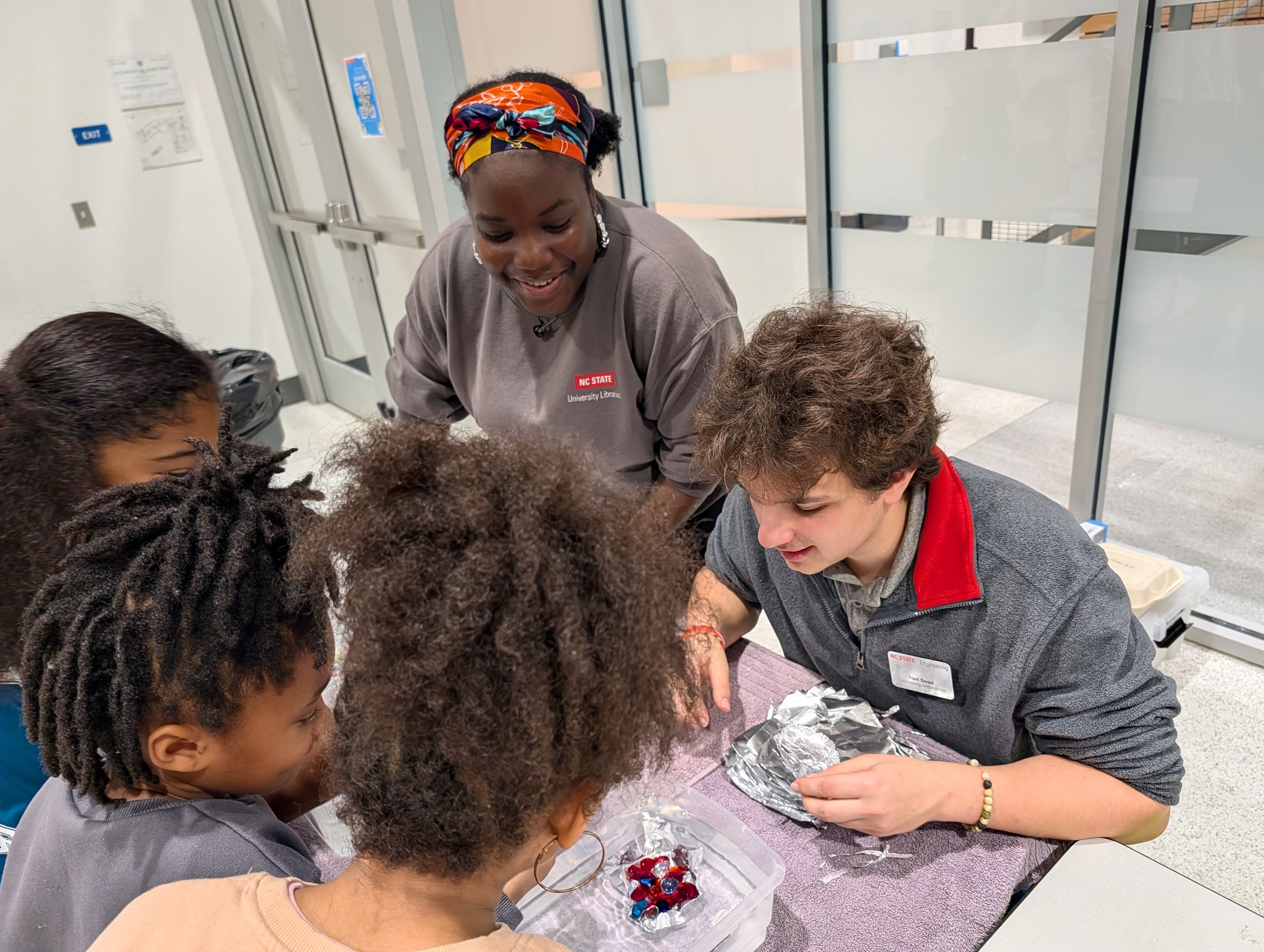 Group learning activity with kids and adults engaging in a fun science experiment at NC State University Library.