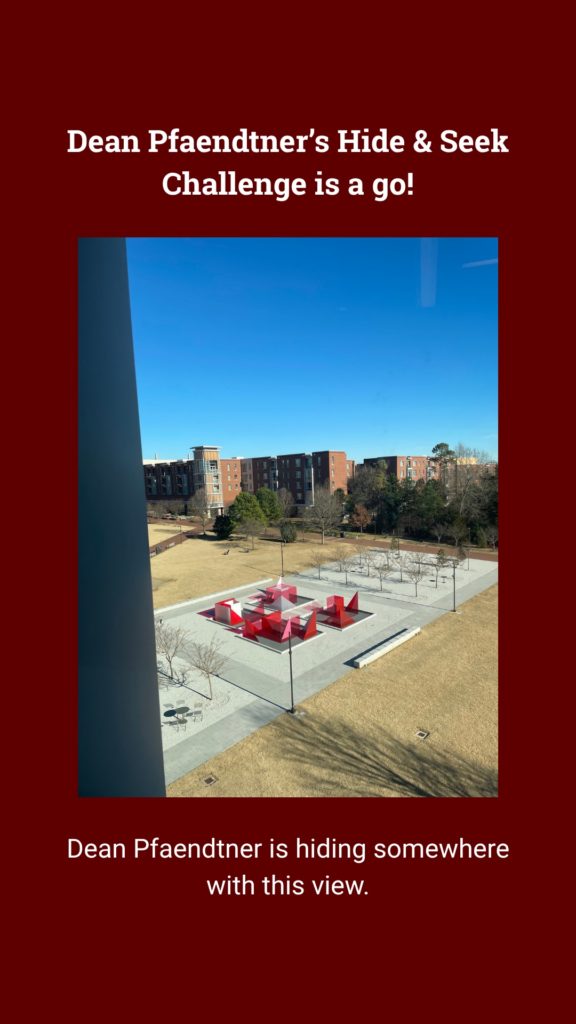 View of a campus courtyard with red structures, trees, and buildings under a blue sky. Hide & Seek challenge setting.