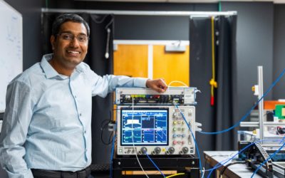 Scientist in lab with advanced equipment, smiling and standing beside an electronic testing device.
