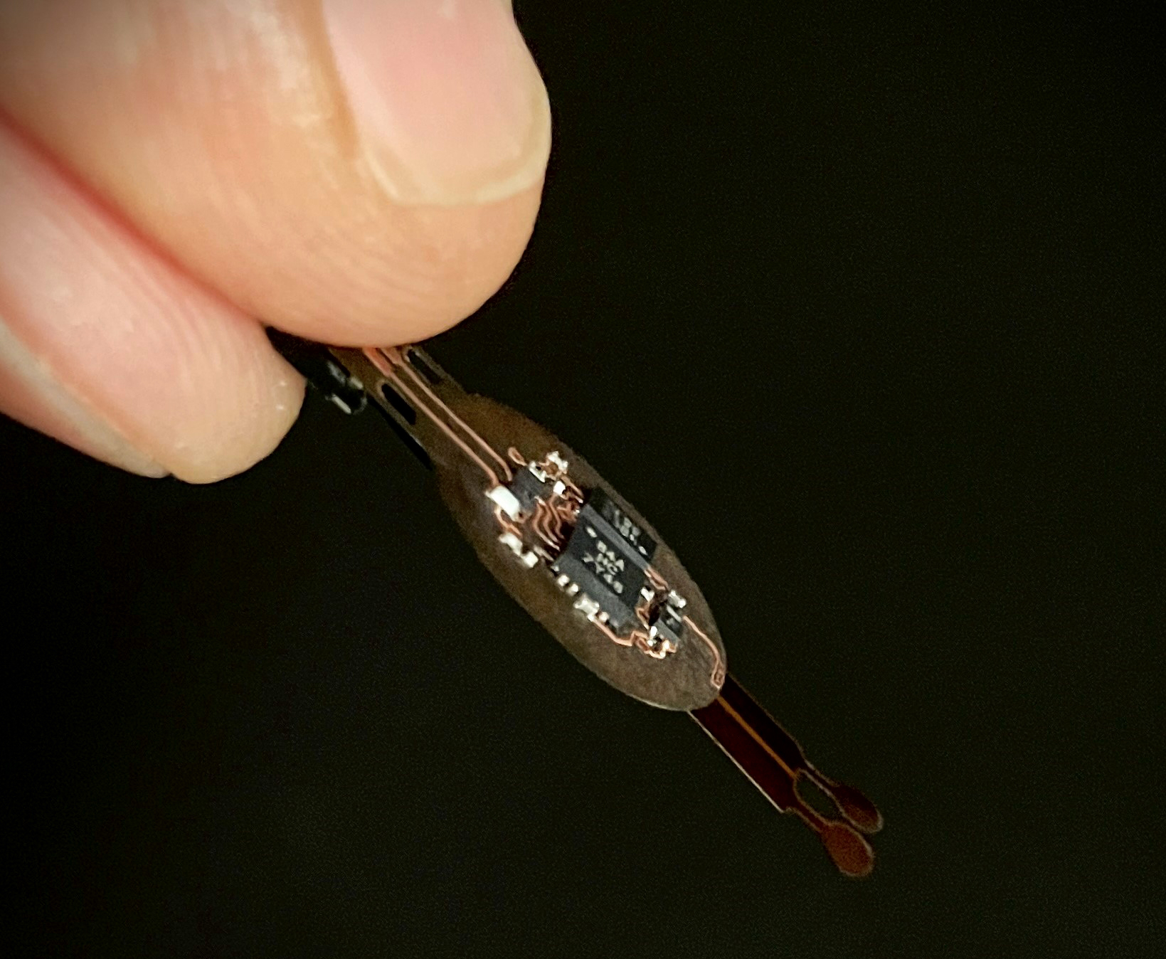 Close-up of a hand holding a tiny circuit board with intricate electronic components against a black background.