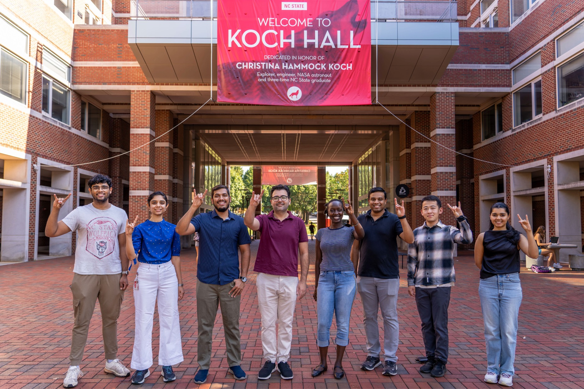 Group of students pose in front of Koch Hall, NC State University, with a welcoming banner above.
